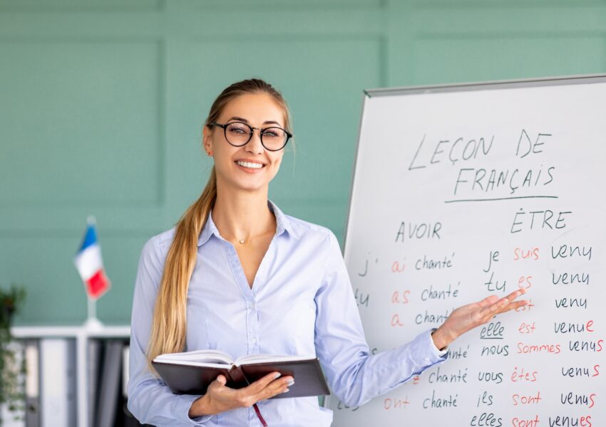 Happy French teacher explaining foreign language rules near blackboard indoors and smiling at camera