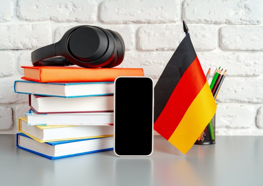 Stack of books and flag of Germany on desk. German language learning concept