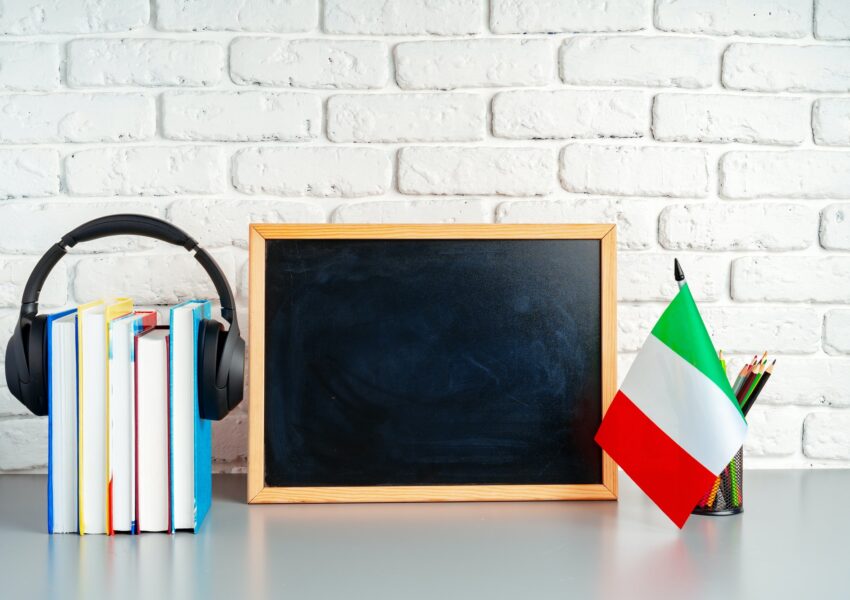 Stack of books, blackboard and flag of Italy on desk. Italian language learning concept