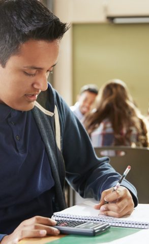 Male High School Student With Calculator Working At Desk